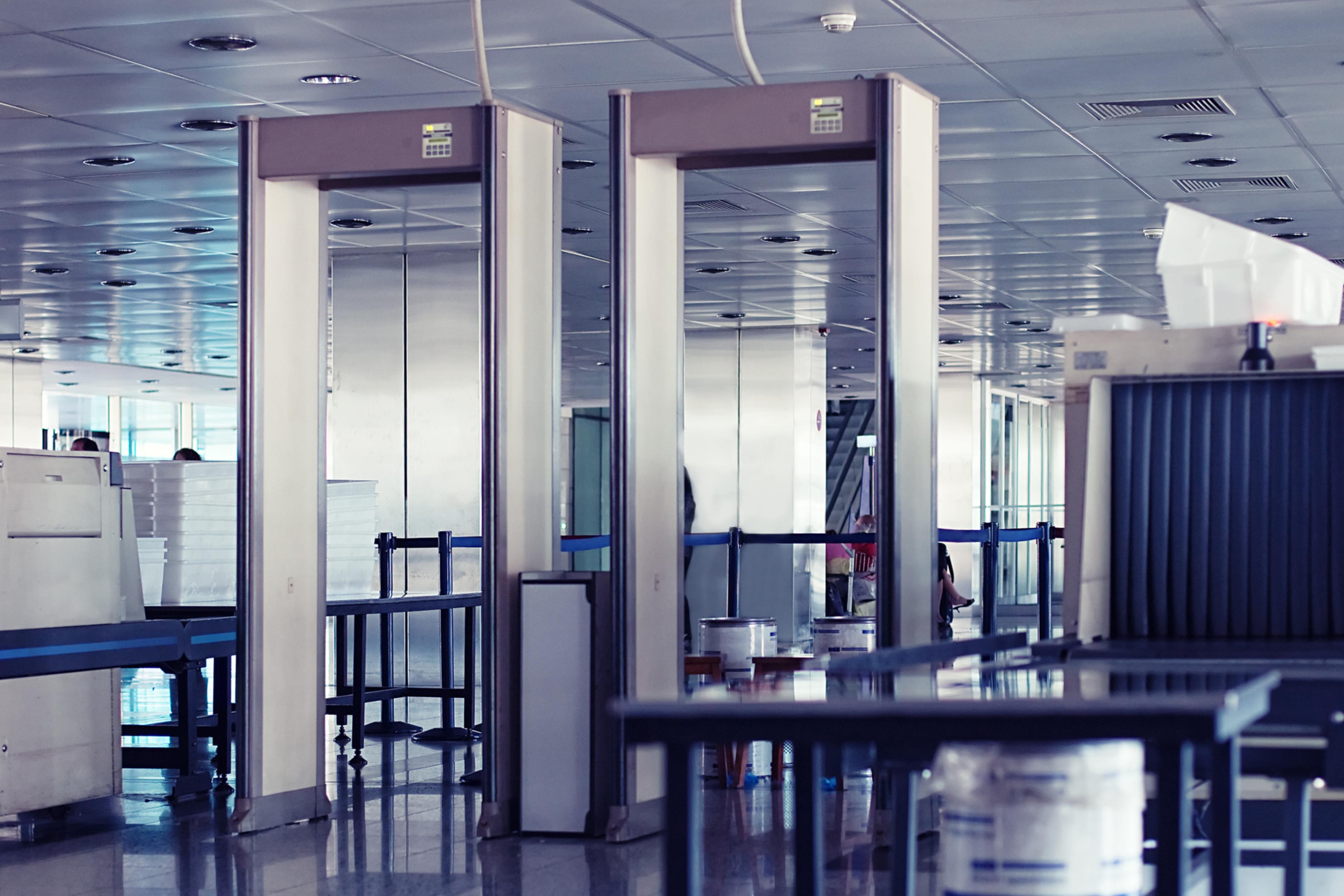 Multiple walk-through metal detector archways and X-ray baggage scanners at a transit hub screening checkpoint