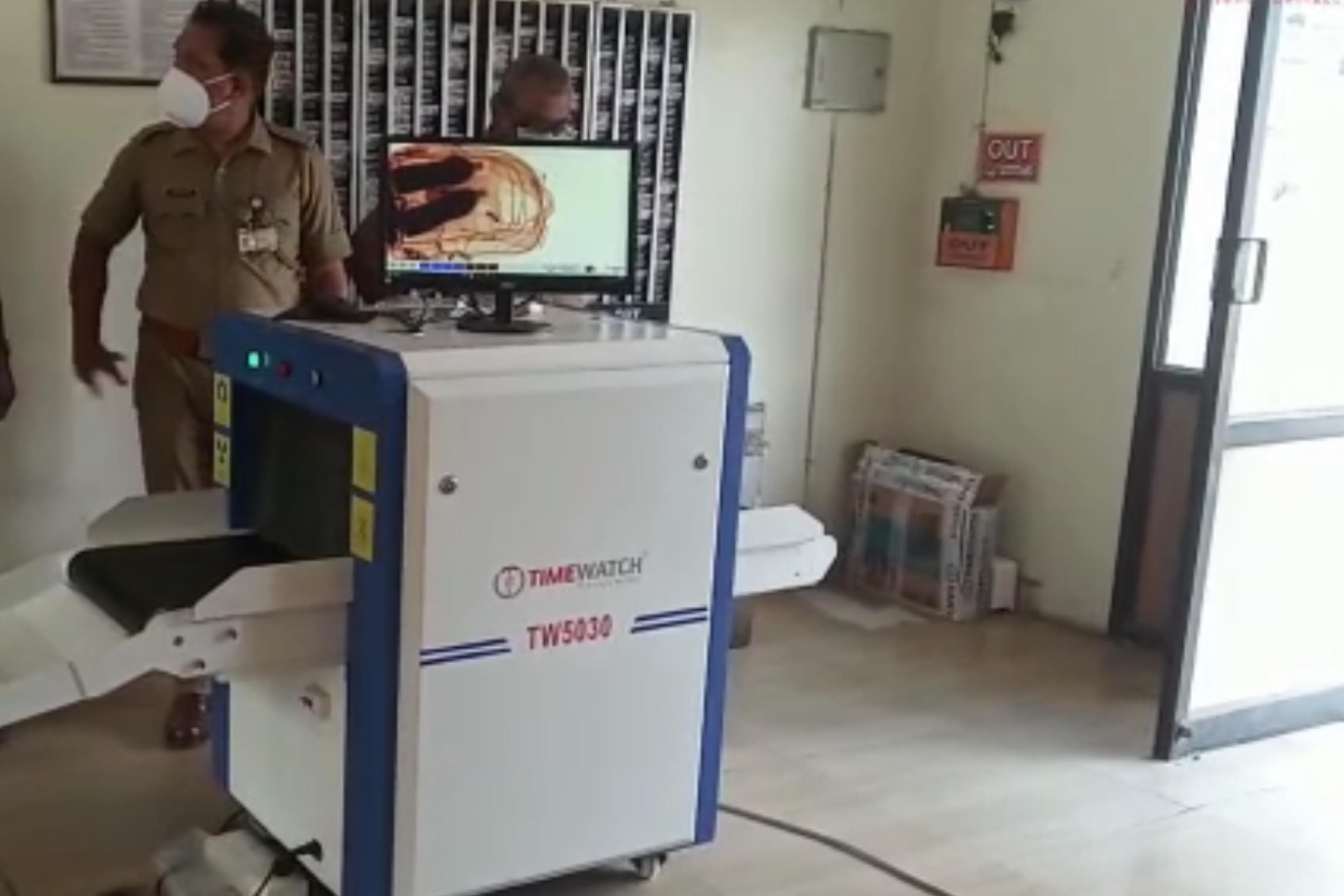TimeWatch TW5030 X-ray baggage scanner in use with a colour-coded scan image on the operator monitor