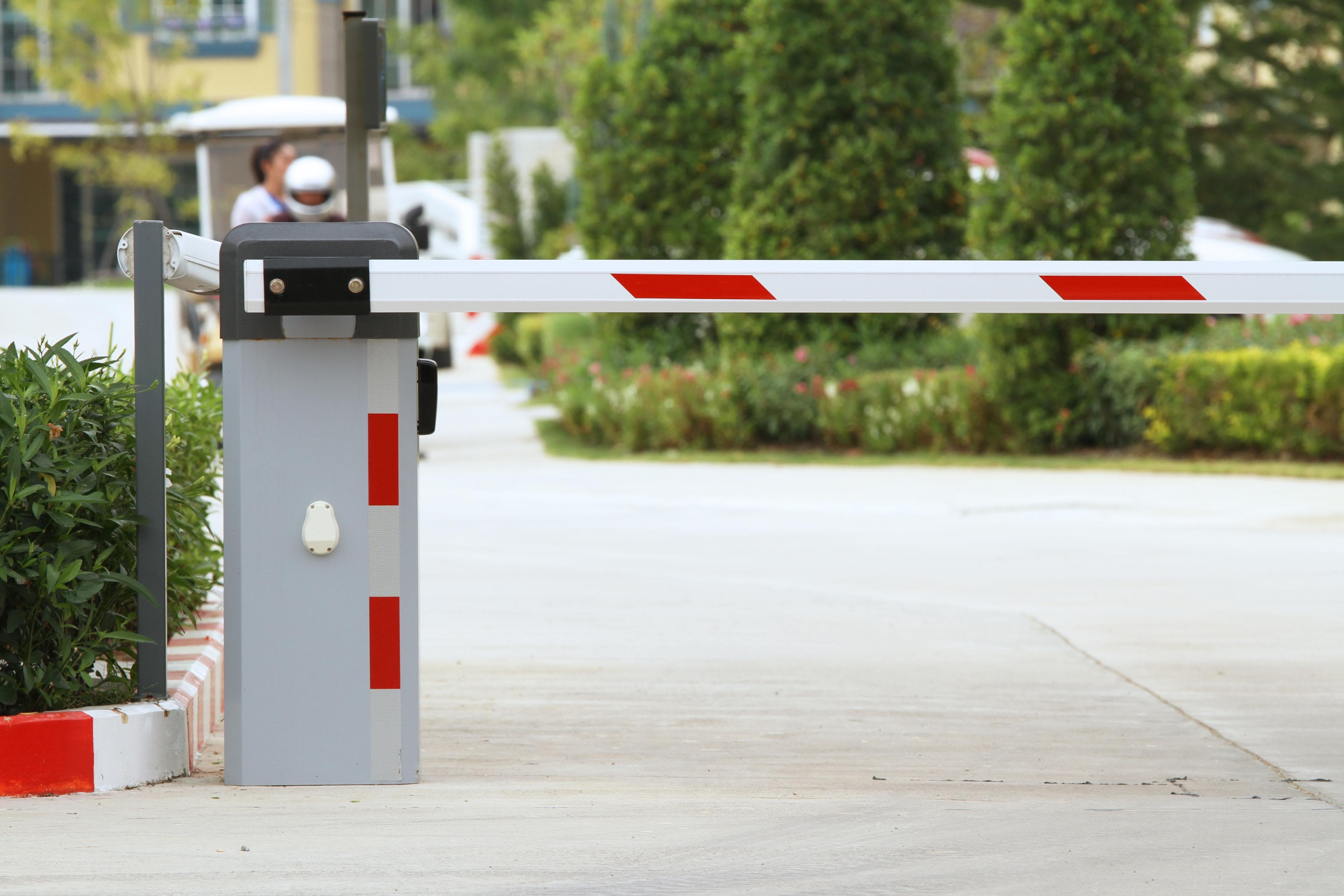 Motorised boom barrier cabinet with its horizontal arm lowered across a driveway lane